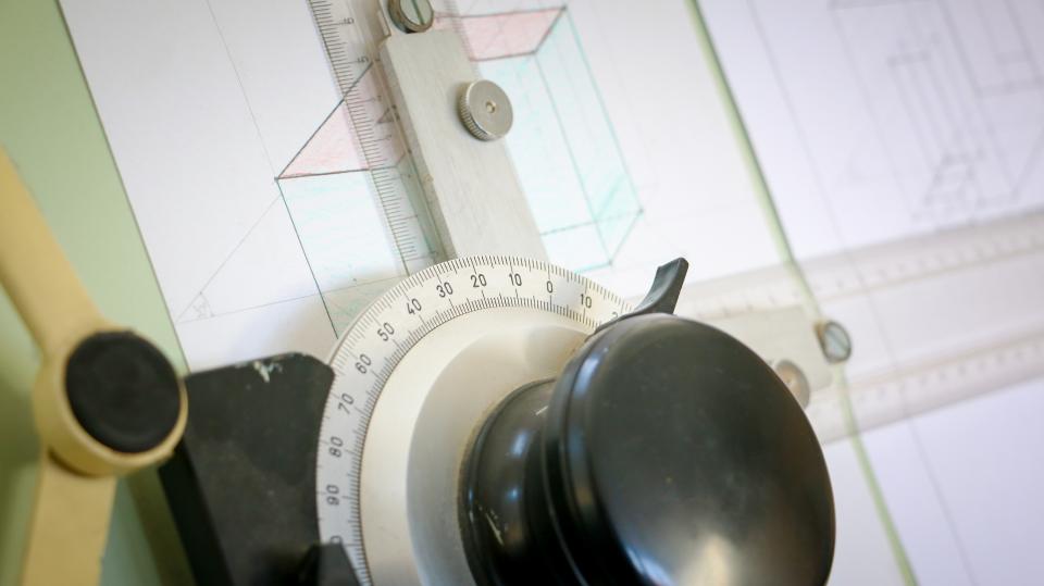 Technical drafting tools and a protractor over an engineering blueprint sketch