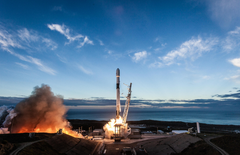 Rocket launching from a coastal launch pad at dusk