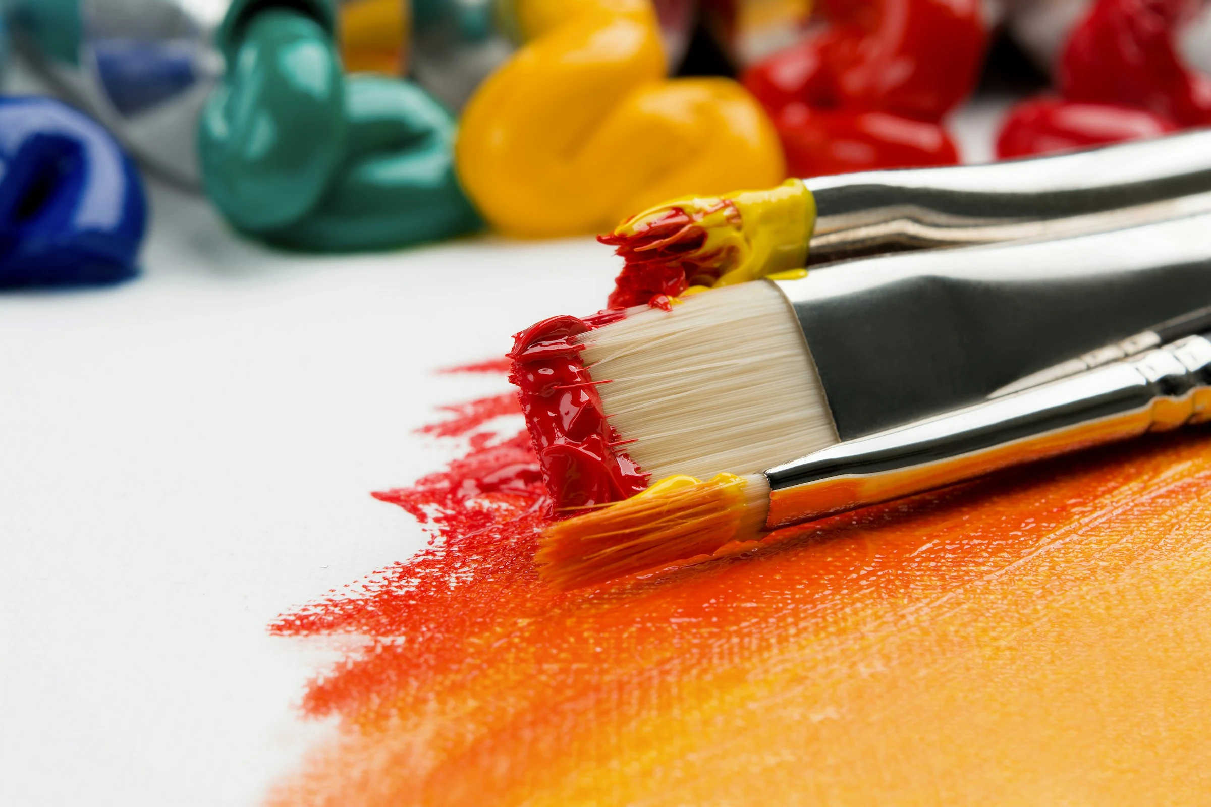 Colorful paintbrushes with wet red and yellow paint on a white canvas