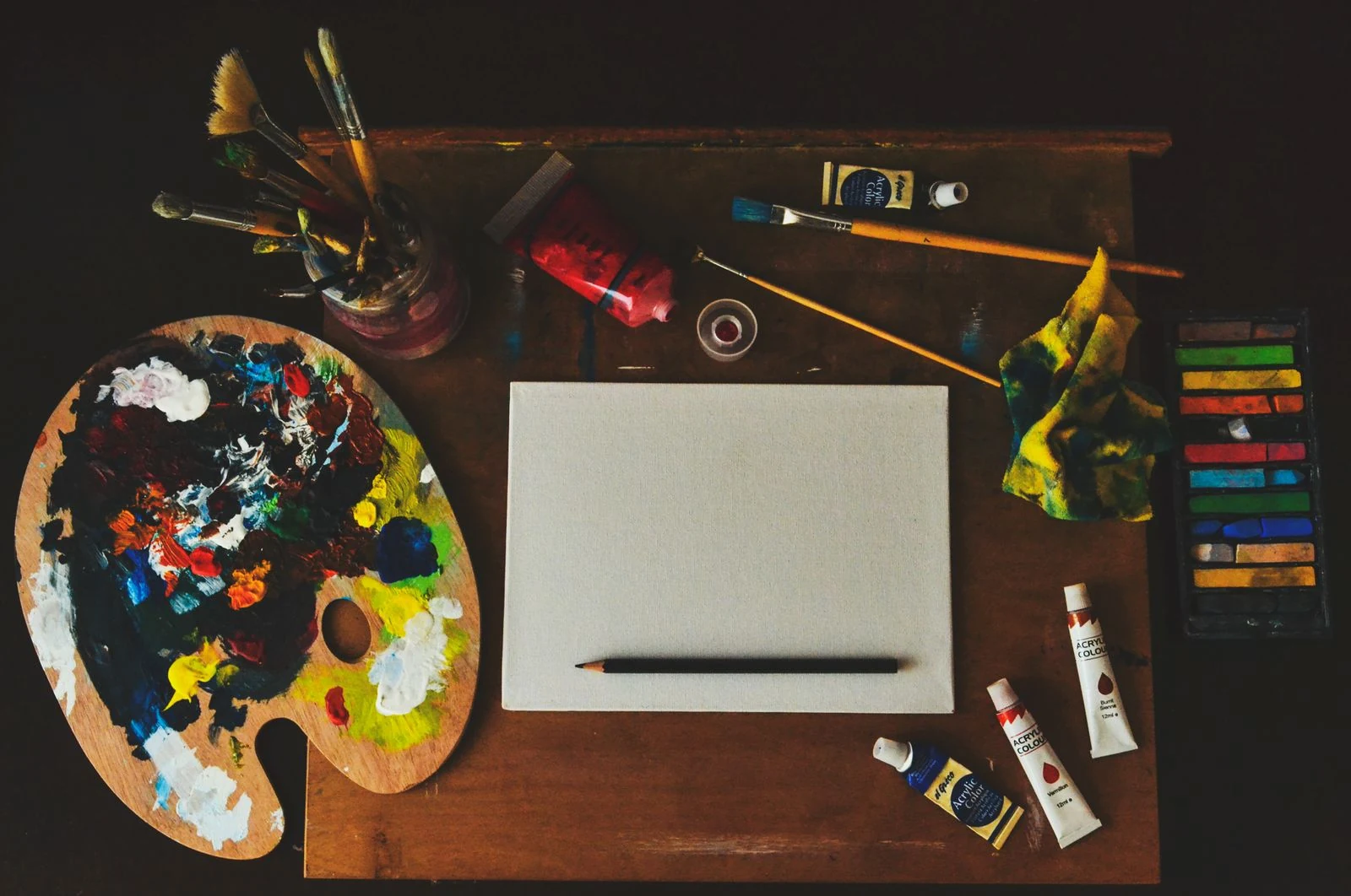 Artist studio flat lay with blank canvas, palette, brushes, and paint tubes