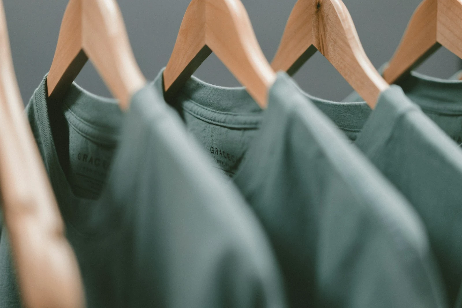 Sage green artist merchandise t-shirts hanging on wooden hangers