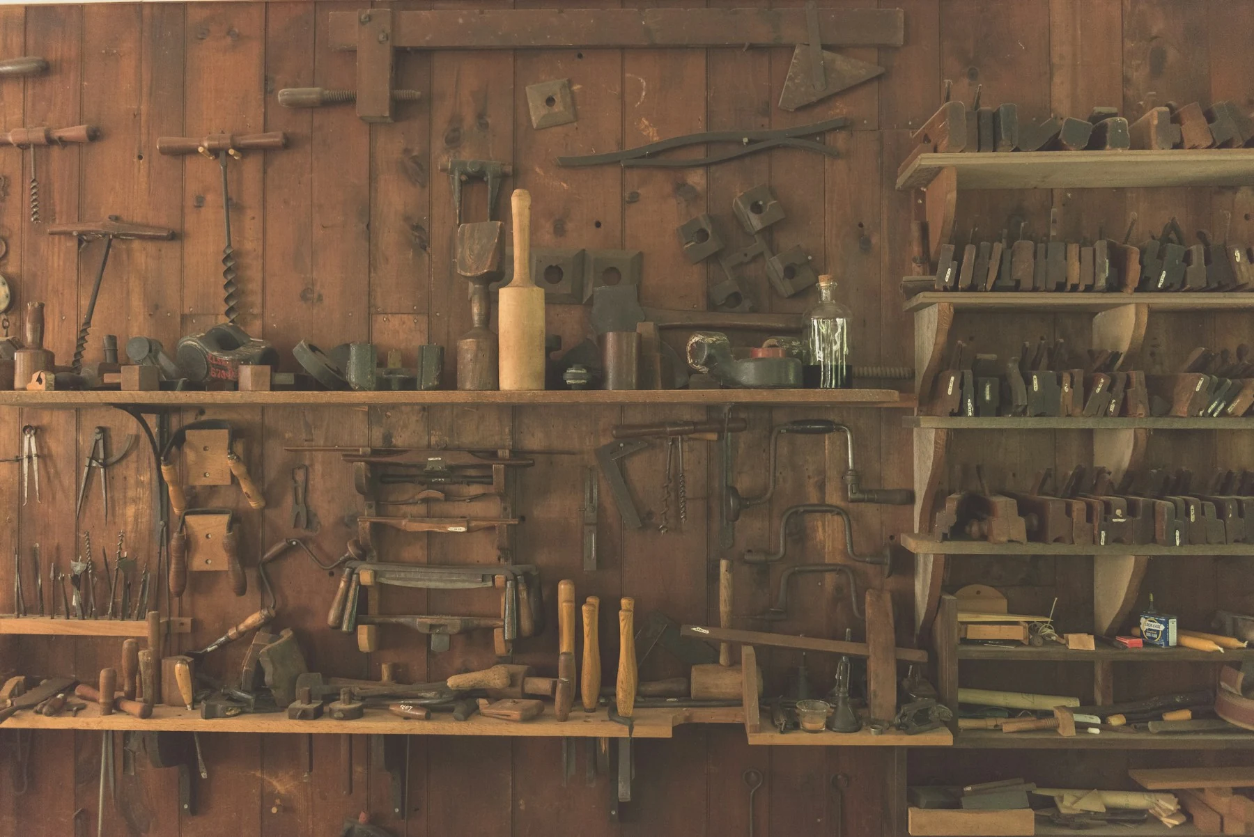 Traditional carpentry hand tools displayed on a wood workshop wall