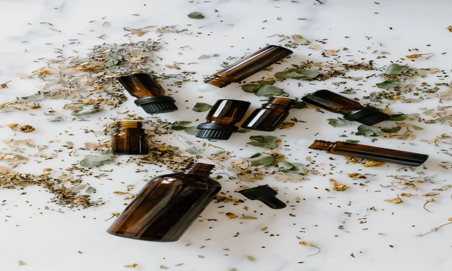 Herbal essential oil bottles surrounded by dried botanical flowers and natural beauty ingredients